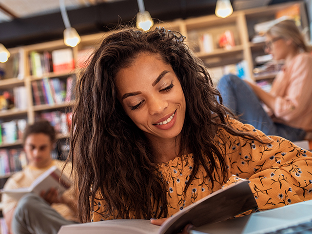 close up of girl in orange blouse reading an open bbok