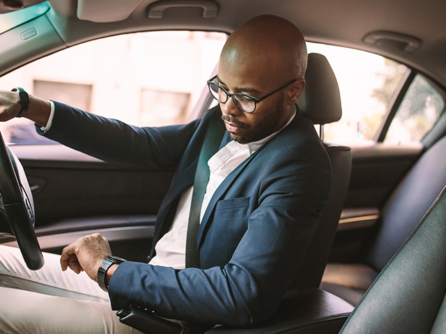 young african male driving a car in traffic looking at wristwatch and checking time