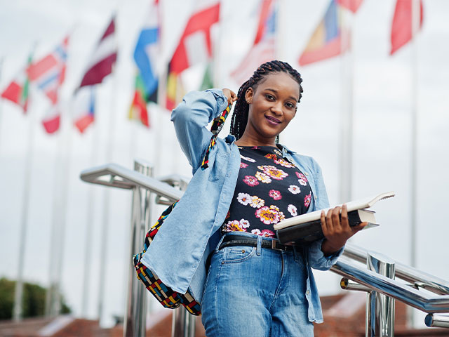 Student holding books in front row of flag poles with various countries flags