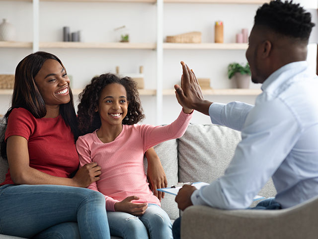 Happy Mother and daughter at an appointment with their social worker. He is giving the young girl a 'high-five'.