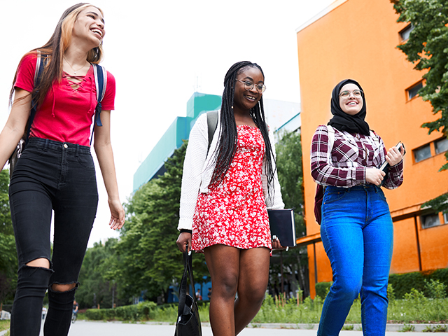 Three young happy female students walking around campus