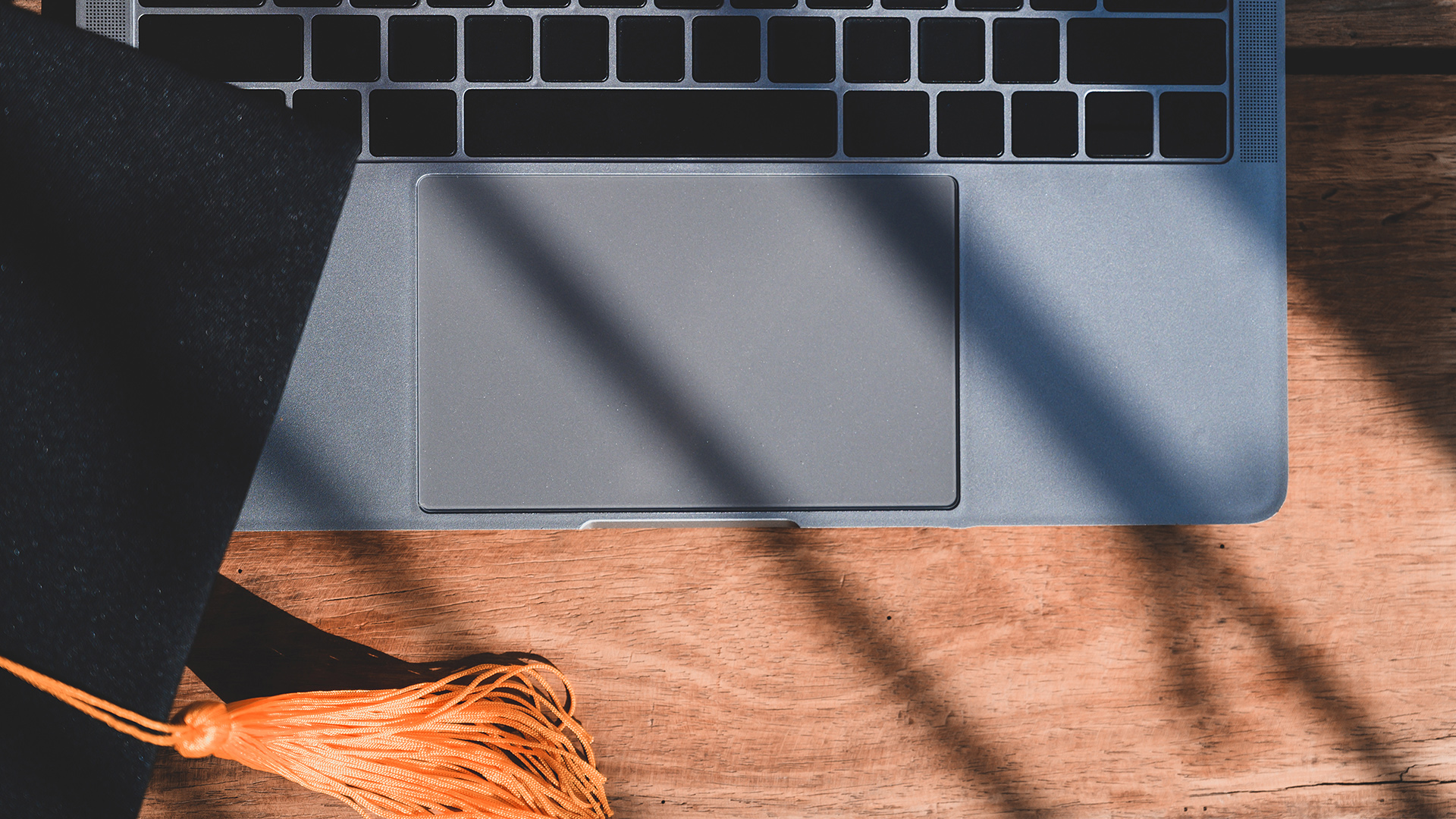 Black Graduation Hat with orange tassle placed on laptop keyboard