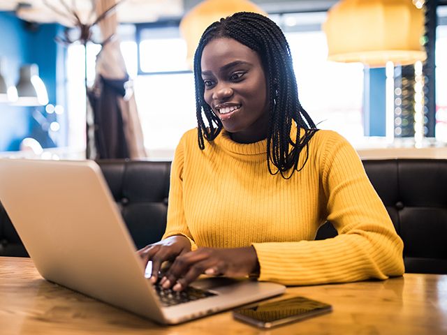 Young black woman student typing on laptop sitting in cafe