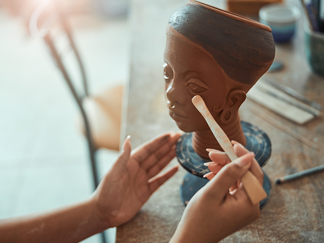 Close up of young womans hands working on African clay sculpture in pottery studio