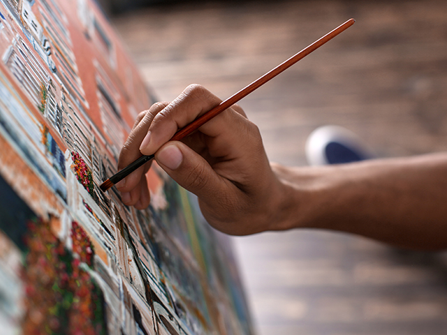  closeup of young African-American artist hands painting picture in workshop